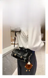Detail of black cylindrical crossbody bag with gold rivets and a brown plush charm