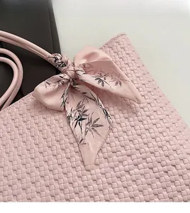 Close-up of pink woven leather tote featuring a floral silk scarf tied on the handle