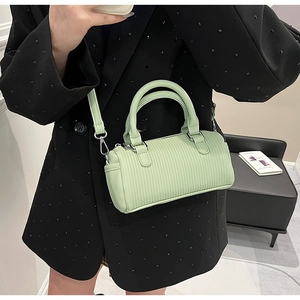 Pale green pleated barrel bag shown worn crossbody with a black blazer for size scale