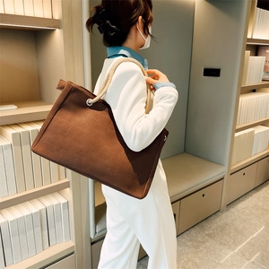 Detail of large brown canvas tote bag with thick cream rope handles worn by model in bookstore