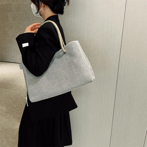 Side view of a grey canvas tote bag with thick cream rope shoulder straps worn by a model