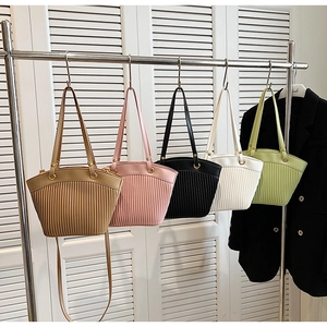 Detail of five pleated tote bags in different colors hanging on a rack in a modern setting