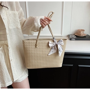 Detail of beige woven tote bag with straw texture and elegant bow scarf accessory
