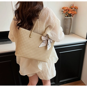 Close-up of beige woven tote bag with a decorative black and white bow on the side