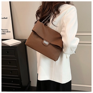 Detail of a brown pleated tote bag with silver buckle worn with a white blazer