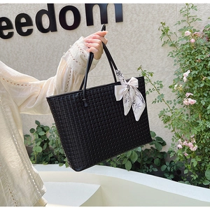 Detail of a black woven tote bag featuring a floral print silk scarf bow on the handle