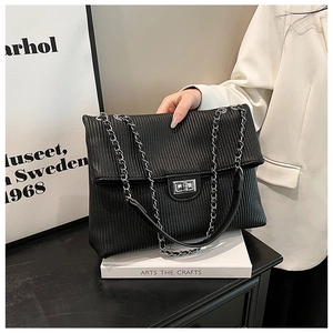 Detail of black pleated tote bag with silver metal twist lock and chain strap