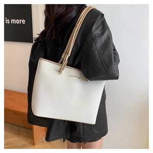 Detail of minimalist cream tote bag with brown handles and gold hardware on a model
