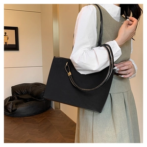 Detail view of black vintage tote bag with gold hardware worn by model in a minimalist room