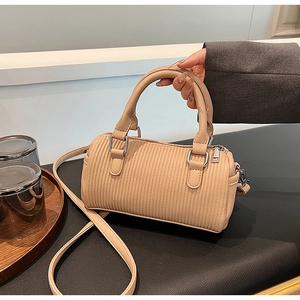 Detailed view of beige pleated barrel handbag with silver hardware and shoulder strap