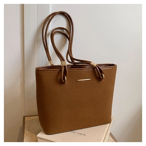 Detailed close-up of brown suede tote bag with leather trim and gold metal buckles