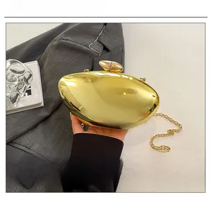 Detail of a golden oval mirror-finish clutch bag with metallic chain and pebble clasp
