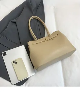 Detail of beige tote bag with metallic turn-lock closure next to a tablet for size reference