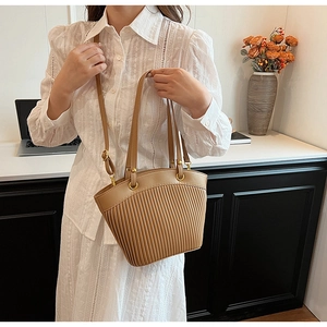Detail of camel tote bag with pleated design and golden hardware on a lace dress model