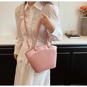 Detail of pink pleated tote bag with golden hardware shown on a white lace dress