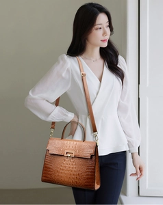 Brown crocodile pattern Kelly bag worn by model with adjustable shoulder strap and gold clasp