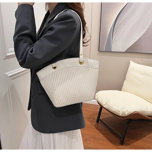 Detail of cream leather tote bag with pleated texture and gold eyelets on a model