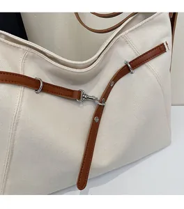 Close-up of cream canvas tote bag showing brown leather strap and metal hardware detail