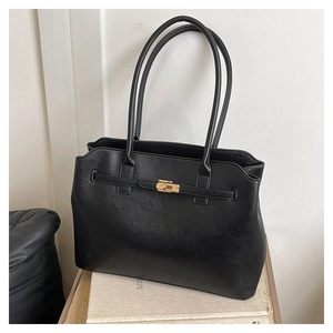 Close-up of a black leather tote bag with gold metal lock and long dual handles