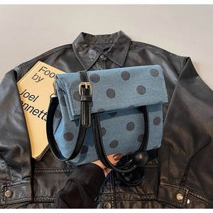 Close-up of blue denim handbag with black polka dots and gold charm accessory detail