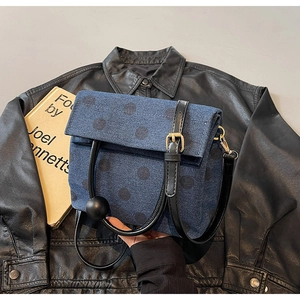 Close-up of blue polka dot denim bag with black round handle on a leather jacket