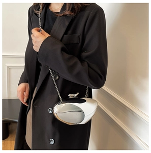 Detail of silver pebble clutch with mirror finish and slim metal chain on black blazer