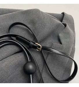 Detail of adjustable black leather strap with gold buckle and unique ball charm accessory