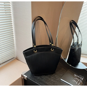 Close-up of black pleated tote bag with golden metal rings on dark wood surface