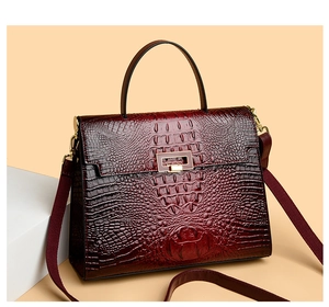 Detail of burgundy crocodile-embossed Kelly handbag with gold lock and wide strap