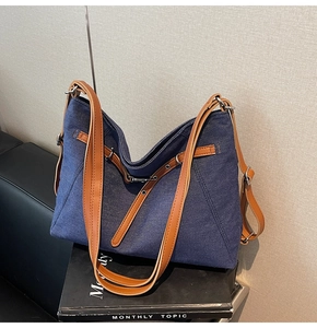 Detail of blue denim tote bag with brown leather straps and metallic eyelet accents