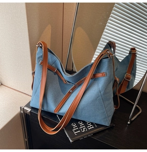 Detail of blue denim tote bag featuring brown leather straps and side cinch design