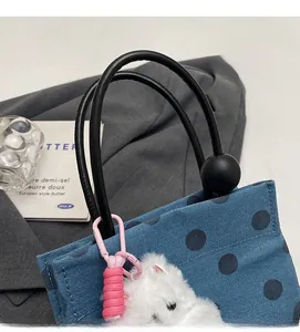 Close-up of blue polka dot canvas tote bag featuring a round black handle and bear charm