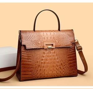Macro detail of brown crocodile-embossed leather and golden hardware lock on Kelly bag