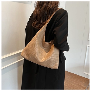 Detailed view of the woven khaki leather hobo bag worn by a model in a minimalist setting