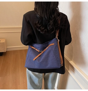 Detail view of denim tote bag with brown leather straps worn over a black blazer
