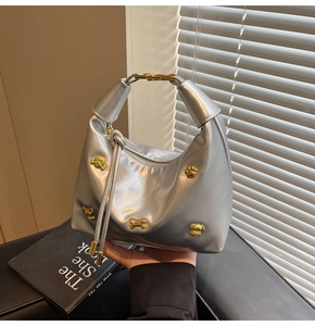 Detail of silver metallic hobo bag featuring golden bear and bone charms with zip closure