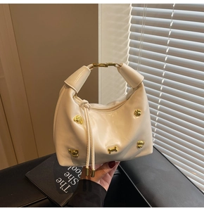 Detail of off-white hobo bag with gold puppy studs and knotted handle in warm light