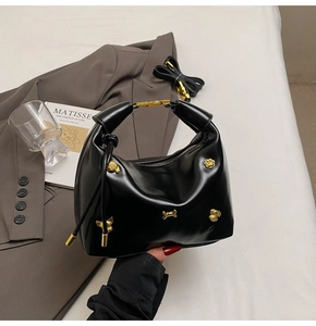 Detail of black glossy leather handbag with gold bone and paw charms in a lifestyle setting