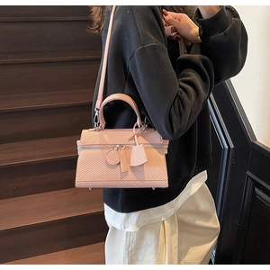 Detail of pink textured crossbody bag with top handle and metal zipper on wooden background