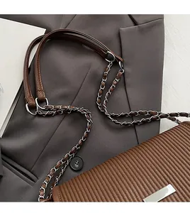 Detail of brown leather strap and silver chain on a quilted shoulder bag over a suit