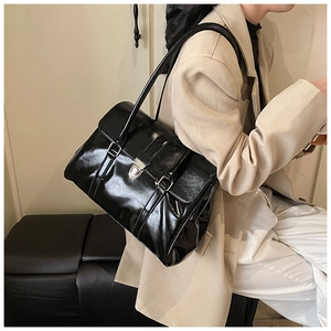 Detail of black glossy shoulder bag with silver metallic buckle on beige blazer outfit