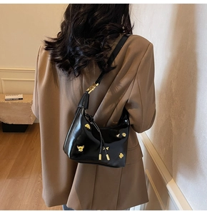 Detail of glossy black shoulder bag featuring gold animal head hardware on a model