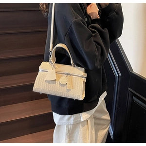 Detail of cream woven shoulder bag featuring textured fabric and decorative charms
