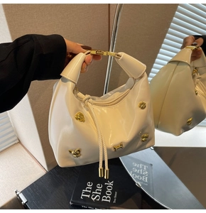 Detail of cream patent leather handbag featuring gold bear studs and metal handle