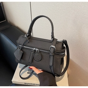 Detail of dark grey cylindrical bag with square embossed texture and adjustable strap