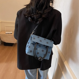 Polka dot denim crossbody bag with circular handles shown on model in a minimalist setting