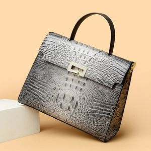 Elegant grey crocodile embossed trapezoid handbag with gold buckle on white stand