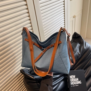 Blue denim tote bag with brown leather straps and silver buckle in a stylish urban setting