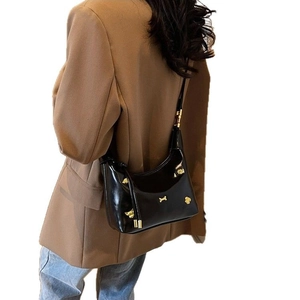 Classic black patent leather shoulder bag with gold metal buckle on a brown suit jacket
