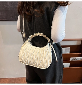 Dettaglio di una borsa a mano matelassé plissettata bianco crema con manico e tracolla sottile